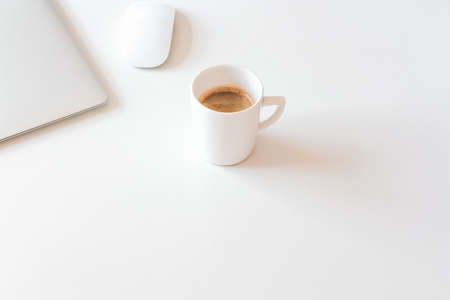 Cup of coffee and silver laptop on white desk. Coffee break in home office concept. の写真素材