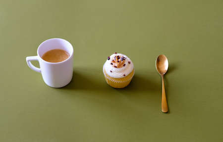 Vanilla cupcakes with cream cheese frosting and white cup of coffee on green background. Sweet food concept. の写真素材