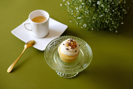 Vanilla cupcakes with cream cheese frosting and white cup of coffee on green background. Sweet food...