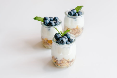 Homemade natural yogurt with granola and blueberries in glass jars on white background. Healthy breakfast set.の写真素材