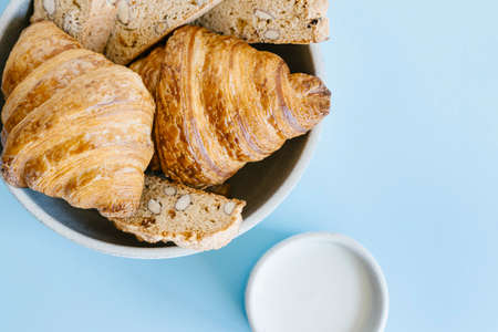 Freshly baked classic croissants and almond biscottis with cup of milk on blue background. Breakfast food concept. の写真素材