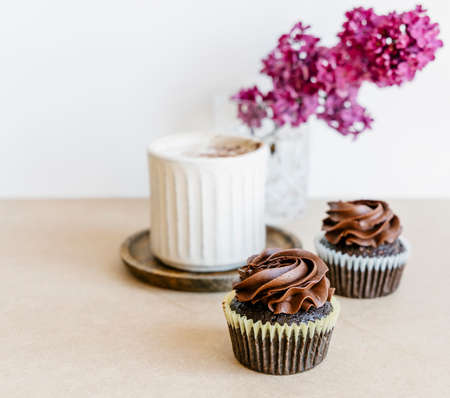 Beautiful lilac flowers, coffee cappuccino and chocolate cupcakes on light background. の写真素材