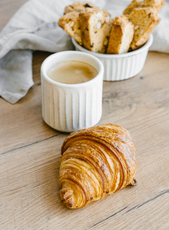 Freshly backed classic croissants and almond biscottis with cup of cappuccino on linen light background. Breakfast food concept. の写真素材