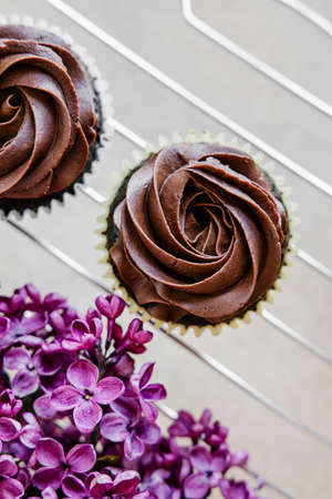 Beautiful lilac flowers and chocolate cupcakes on light background. の写真素材