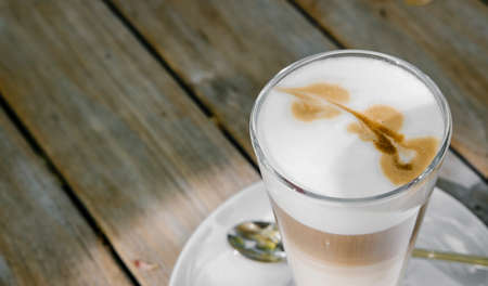 Coffee cappuccino or latte in tall glass on wooden table in outdoor garden.の写真素材