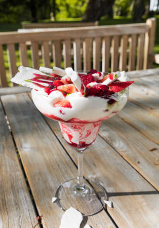 Traditional summer dessert Eton mess. Mixture of meringue, whipped cream, fresh strawberries and raspberries, decorated with mint sauce on wooden table background.の写真素材