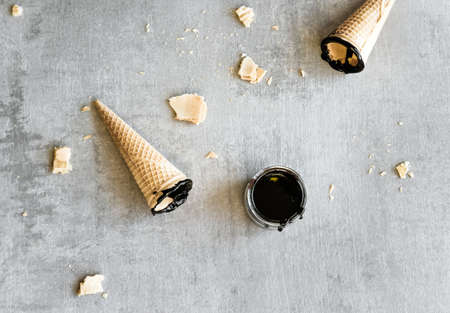 Homemade dark chocolate sauce in glass jars, ice cream waffle cones on gray background. の写真素材
