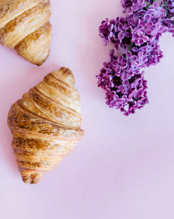 Freshly baked classic croissants and lilac flowers on pink background. Breakfast food concept.の写真素材