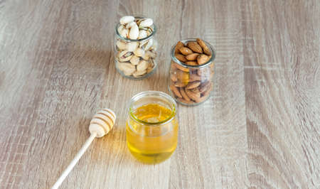 Honey in glass jar with wooden honey dipper and almonds, peanuts on light wooden table background. の写真素材