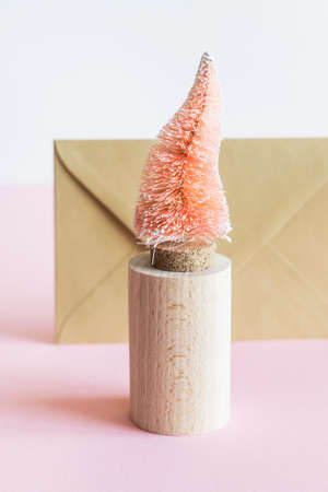 Coconut fiber orange Christmas tree on wooden stand, kraft paper envelope on pink white background, zero waste festive concept.の写真素材