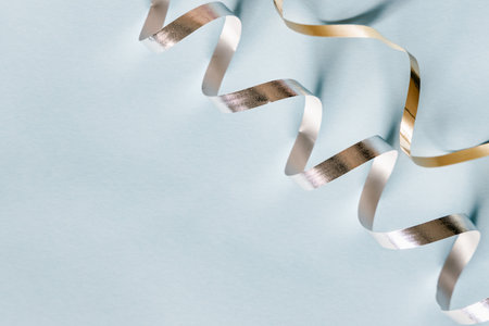 Silver and golden festive ticker tape decoration on pastel blue background. Holidays modern...