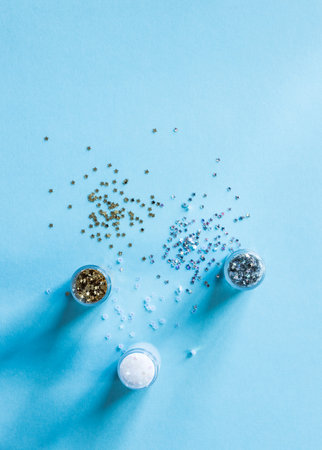 Plastic containers with metallic shiny silver, golden and pearly white stars shaped glitters on blue...