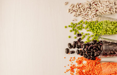 A set of different dried legumes is in glass cups and is a little scattered: red lentils, green...