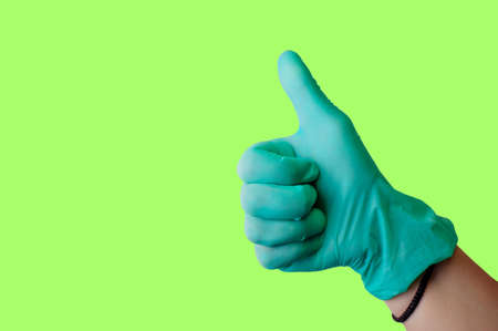 Female hand in blue latex glove makes thumbs up like gesture isolate on a malachite background. Medical health concept. Copy spaceの写真素材