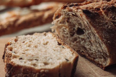 dark yeast-free buckwheat bread in a cut lies on a cutting wooden board on a wooden table next to italian grissini on a linen tablecloth in rustic style. Selective focus. Concept of making breakfast.の写真素材