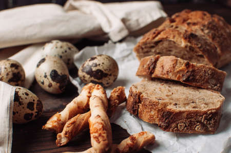 set dark yeast free buckwheat bread in a cut lies on parchment, next to quail eggs and Italian grissini. The concept of preparing breakfast.の写真素材