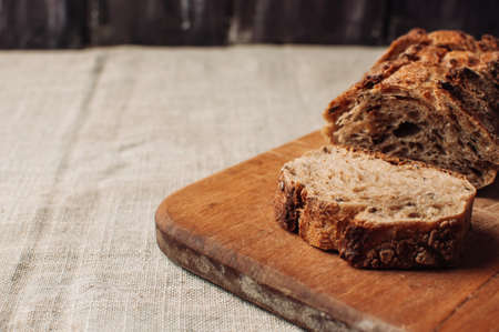 dark yeast-free buckwheat bread in a cut lies on a cutting wooden board on a wooden table covered with a linen tablecloth in a rustic style. Breakfast cooking concept.の写真素材