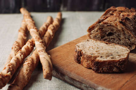 dark yeast-free buckwheat bread in a cut lies on a cutting wooden board on a wooden table, next to it is Italian grissini on a linen tablecloth in a rustic style. Breakfast cooking concept.の写真素材