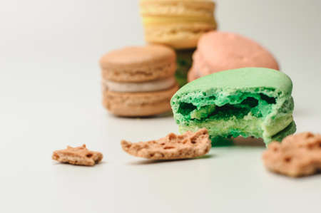 one green macaroon in the foreground lies a bite. Nearby are crumbs from a French pastry. In the background, three fresh colored macaroons lie in a pile. Meringue on an isolated backgroundの写真素材