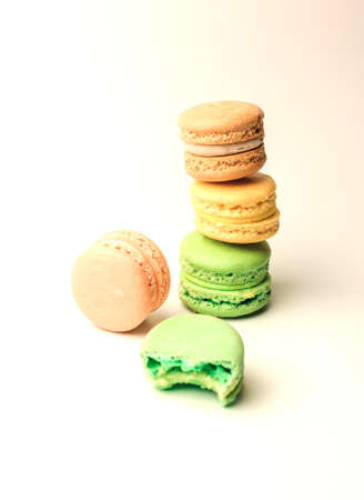 Detail of delicious brown, green and yellow macaroons stacked in a pile on a white background, next to a bitten piece of green cake lies.の写真素材