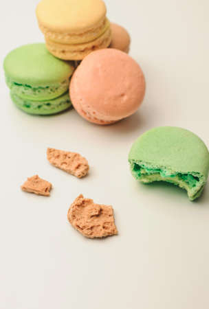 one green macaroon in the foreground lies a bite. Nearby are crumbs from a French pastry. In the background, three fresh colored macaroons lie in a pile. Meringue on an isolated backgroundの写真素材