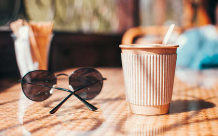 Disposable paper coffee cup with holder on table in cafe with wooden stirrer,near sunglasses.Environmentally friendly lifestyle.Zero Waste,Save The Planet,Earth Day,No Plastic,Recycling Conceptの写真素材