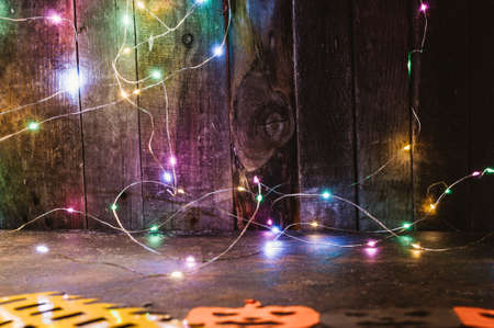 Color LED garland on a wooden wall and pumpkins carved from orange paper on the table. copy space. Crafts for halloween celebration concept. Handwork.の写真素材