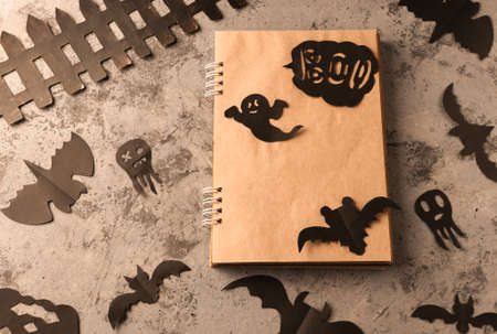 Figures from a black bat and ghosts carved from black paper on a concrete surface. Notepad with craft sheets and copy space. Crafts for halloween celebration concept. Handwork. Flat layの写真素材