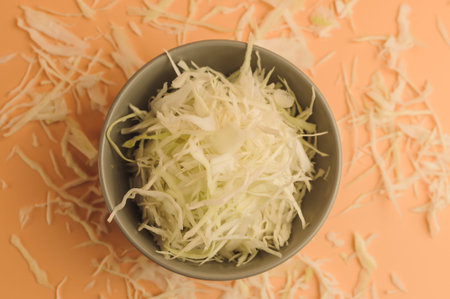 Finely chopped white cabbage on beige background,cabbage in bowl and around on the surface,chopped...