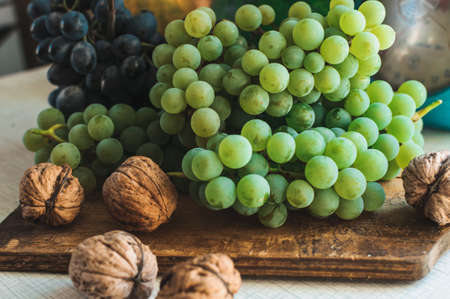 Autumn still life with grapes on a wooden board and walnuts around on a wooden white table. On the back scales. The concept of autumn harvest. Happy Thanksgiving. Selective focus. Template for design.の写真素材