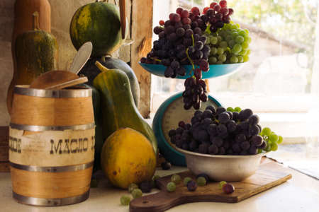 Autumn still life with pumpkins, melons, watermelon, grapes on a scale and in a metal bowl on a wooden white table. Autumn harvest concept. Happy Thanksgiving. Selective focus. Template for design.の写真素材