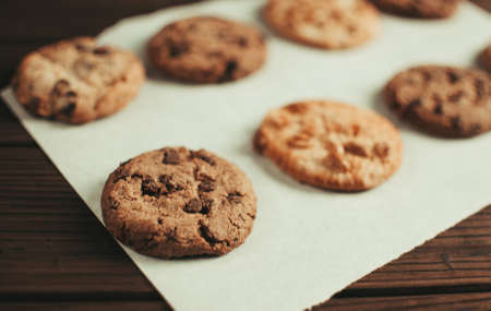 Chocolate covered cookies lay on a parchment paper in a row. Gluten-free cookies on a wooden table out of the oven. Selective focusの写真素材