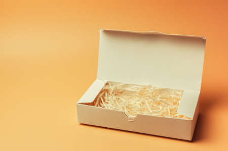 Open gift white box inside with paper hay on a beige background, isolate. Copyspace. The concept of sales, discounts, Christmas gifts and shopping.の写真素材