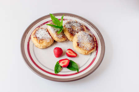 Gourmet breakfast - cottage cheese pancakes, cheesecakes, cottage cheese pancakes with strawberries, mint and powdered sugar in a white plate. Useful dessert on white background isolateの写真素材