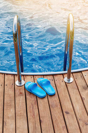 Slippers by the pool with a staircase and a wooden terrace in the hotel. The concept of the arrival of summer and swimming.の写真素材