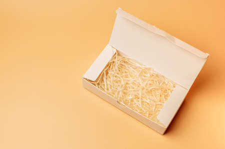 Open gift white box inside with paper hay on a beige background, isolate. Copyspace. The concept of sales, discounts, Christmas gifts and shopping.の写真素材
