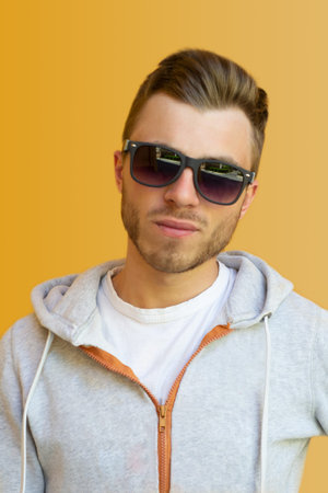 young hipster in sunglasses against a yellow wall on the street. A guy in a white T-shirt, sweater...