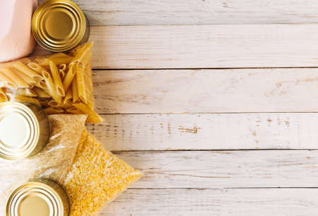 Food supplies quarantine food crisis isolated on white wooden background. Rice, pasta, corn flakes, toilet paper, canned food. Concept of food delivery, donation, charity. Copyspace.の写真素材