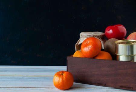 Food delivery during quarantine and isolation. Products folded in a box on a wooden white table background. Fruits vegetables, canned goods, cereals. Concept of donation and mercy. Copy space.の写真素材