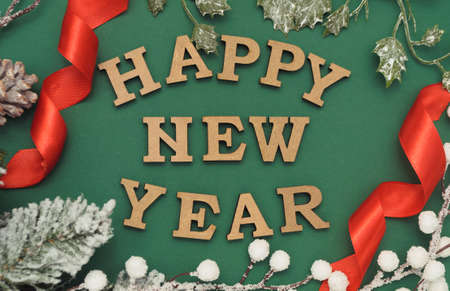Wooden letters Happy New Year and numbers 2021. Congratulation card with the holiday on a green background with red ribbons, fir branches and holly. Festive party decoration. top view. flat layの写真素材