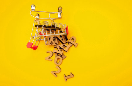 Happy New Year 2021 is approaching. Wooden letters fell from a grocery cart on a yellow background. Festive decoration or postcard concept. Top view and flat. Copy spaceの写真素材