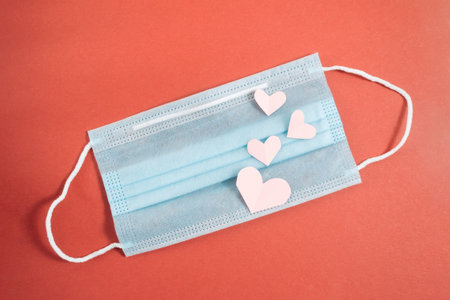 COVID-19. Face mask with cut paper heart on a red background. Medical masks to protect against viruses and pollution. Concept of celebrating valentines day in a new reality.の写真素材