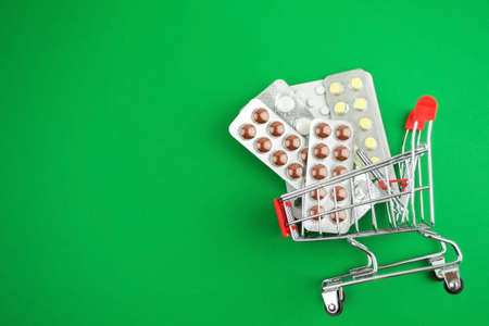 capsules, pills, medicines in blisters on green background in shopping cart. Pharmacy, people and health concept.Online ordering of medicines, online shopping.Vitamins and dietary supplements.Copy space.の写真素材