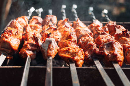 Cooking marinated pork skewers on the grill. Juicy pieces of meat in the marinade are covered with smoke from the fire. Fried pork kebab on an open fire. Grill cooking season.の写真素材