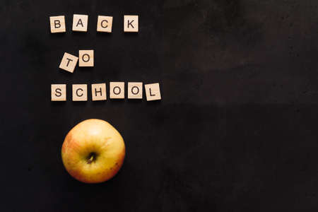 black graphite board with wooden letters back to school and a ripe yellow apple. copy spaceの写真素材