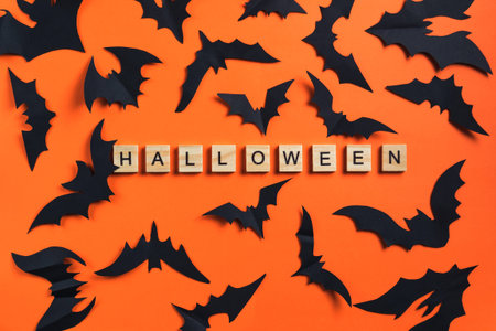 The inscription from wooden cubes and bats cut from black paper on an orange background. Halloween...