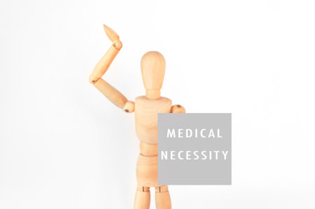 A wooden figure is holding a sign that says Medical Necessity. Concept of urgency and importance, as the figure is reaching out to the viewer with the signの写真素材