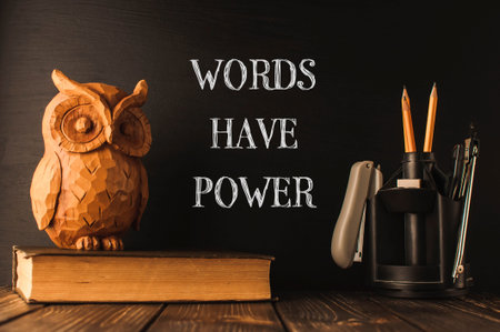 A wooden owl sits on top of a stack of books. The owl is surrounded by writing that says Words have power. The image conveys the idea that words can have a significant impact on peopleの写真素材