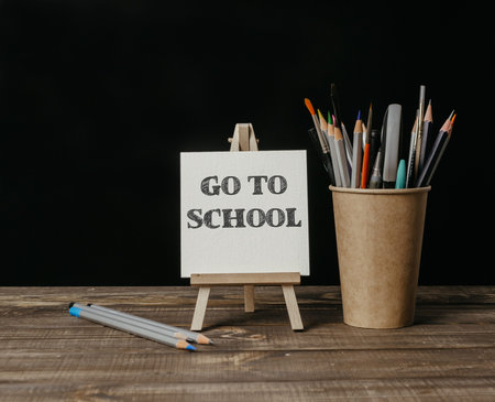 A wooden desk with a white sign that says Go to School and a cup of pencils. High quality photo