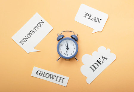A clock sits on a table with a bunch of paper with words like growth, plan, innovation, idea and...